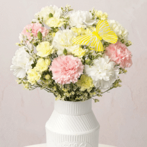 Buttercream Bliss Letterbox bouquet from Bunches featuring pastel pink, cream, yellow and white carnations with a decorative butterfly pick arranged in a vase